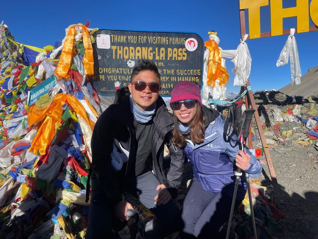 Trekkers posing at Thorong La Pass sign with prayer flags on the Annapurna Circuit, a key highlight often discussed in Annapurna Base Camp Trek vs Annapurna Circuit Trek comparisons.