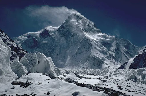 Snow-covered K2 mountain peak in Pakistan with strong winds blowing snow off the summit, captured in the Karakoram range.