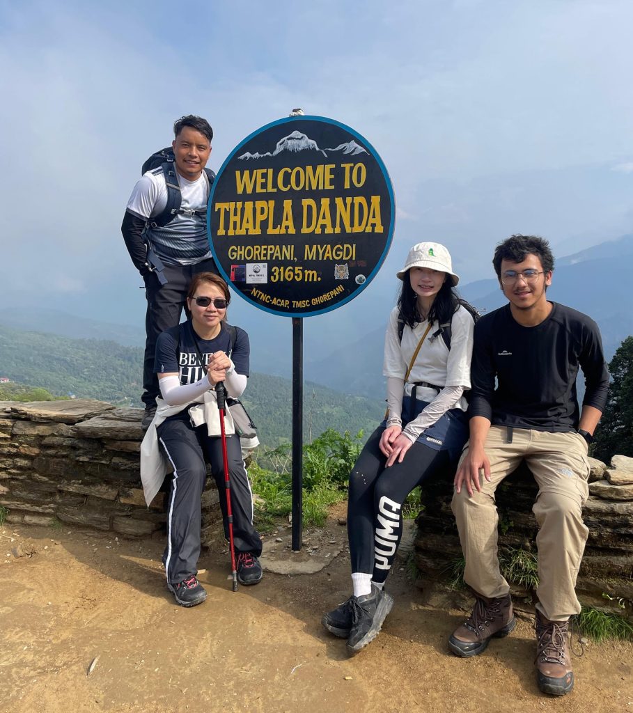 Trekkers posing beside the welcome sign at Thapla Danda (3,165 m) during a side trip on the Annapurna Base Camp Trek in Nepal.