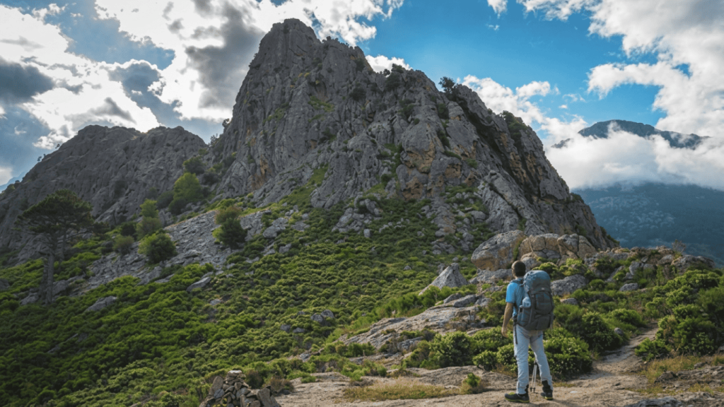 Hiker exploring rugged mountain terrain on the GR20 Trail with dramatic rocky peaks and lush green landscape