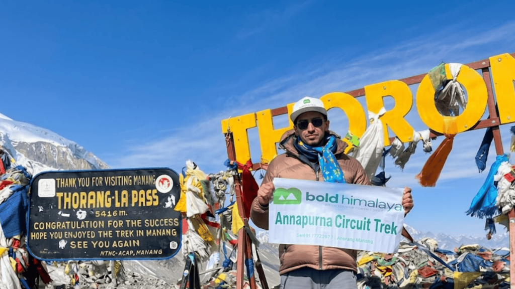 Trekker at Thorong La Pass 5416m holding Bold Himalaya Annapurna Circuit Trek banner in Nepal Himalayas
