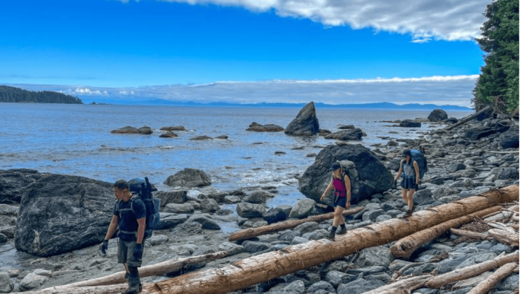 Hikers crossing rocky shoreline on the West Coast Trail along the Pacific coast with ocean views