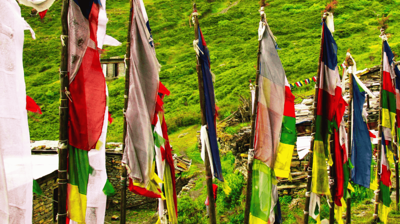 Colorful Buddhist prayer flags hanging on poles in a green Himalayan village landscape in Nepal