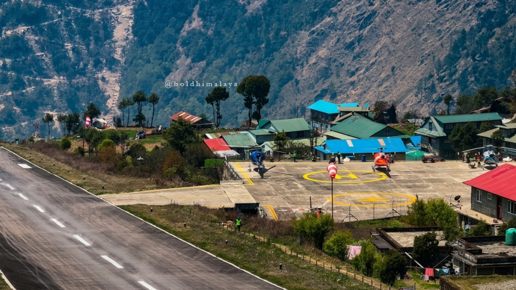 Helicopters parked on the helipad at Lukla Airport in Nepal, with colourful buildings, mountain terrain, and clear Himalayan weather conditions