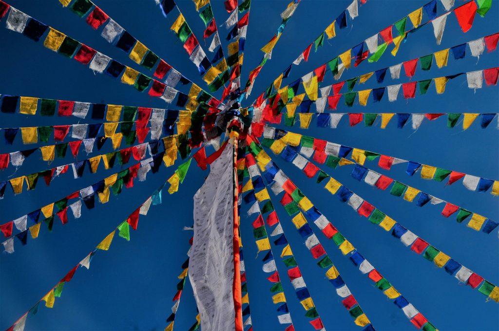 Colorful Tibetan prayer flags radiate from a central pole beneath a clear blue sky.