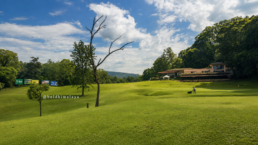 Golf course in Nepal with lush green fairways, a clubhouse surrounded by forested hills.
