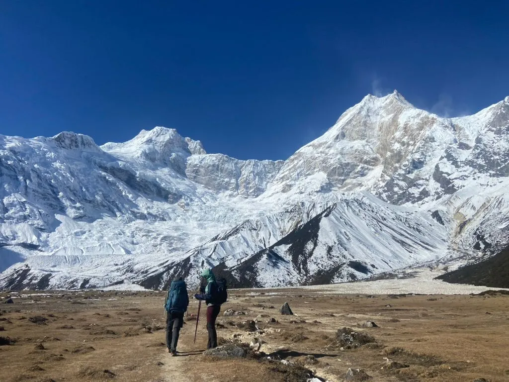 Trekkers walking toward snow-covered Mount Manaslu, during Manaslu Circuit Trek 14 days.
