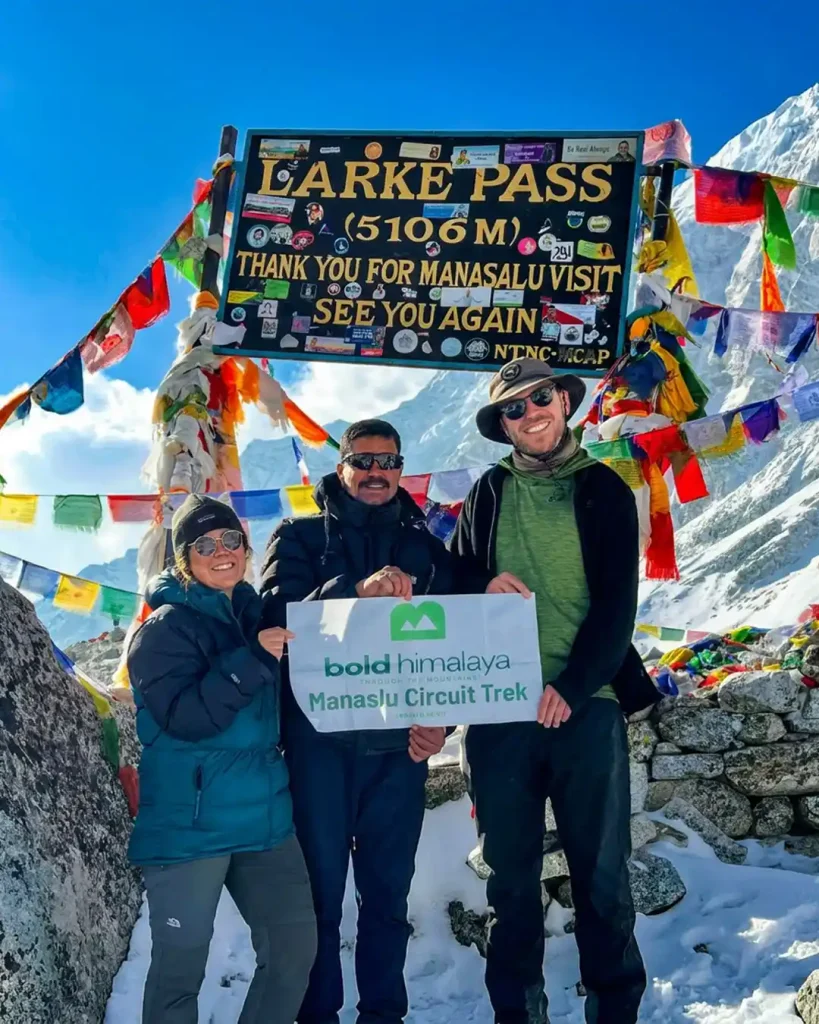 Three trekkers stand at Larke Pass in the snowy Himalayas.